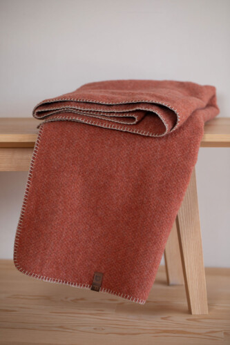 MERANO Kuscheldecke in Terracotta Rot locker über eine Sitzbank drapiert – gemütliches, modernes Wohnzimmer