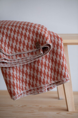 MERANO Kuscheldecke in Hahnentrittmuster Terracotta Rot locker über eine Sitzbank drapiert – gemütliches, modernes Wohnzimmer